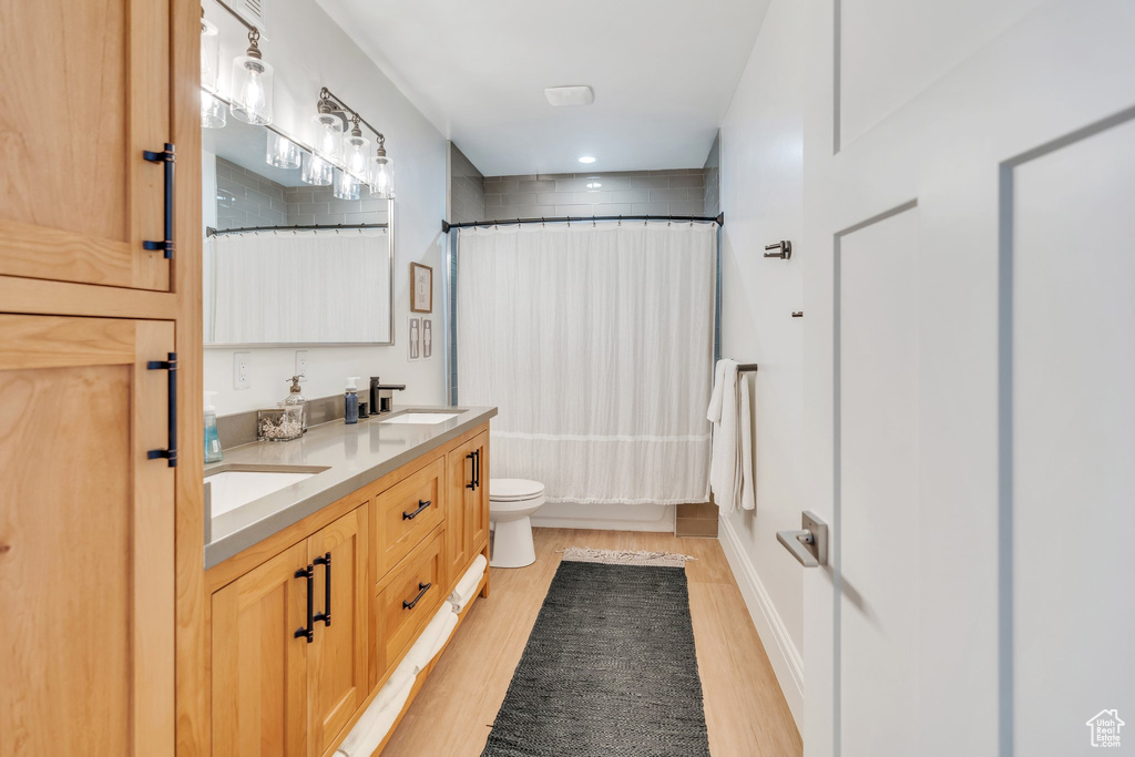 Bathroom featuring wood finished floors, double vanity, shower / bath combo with shower curtain, and recessed lighting