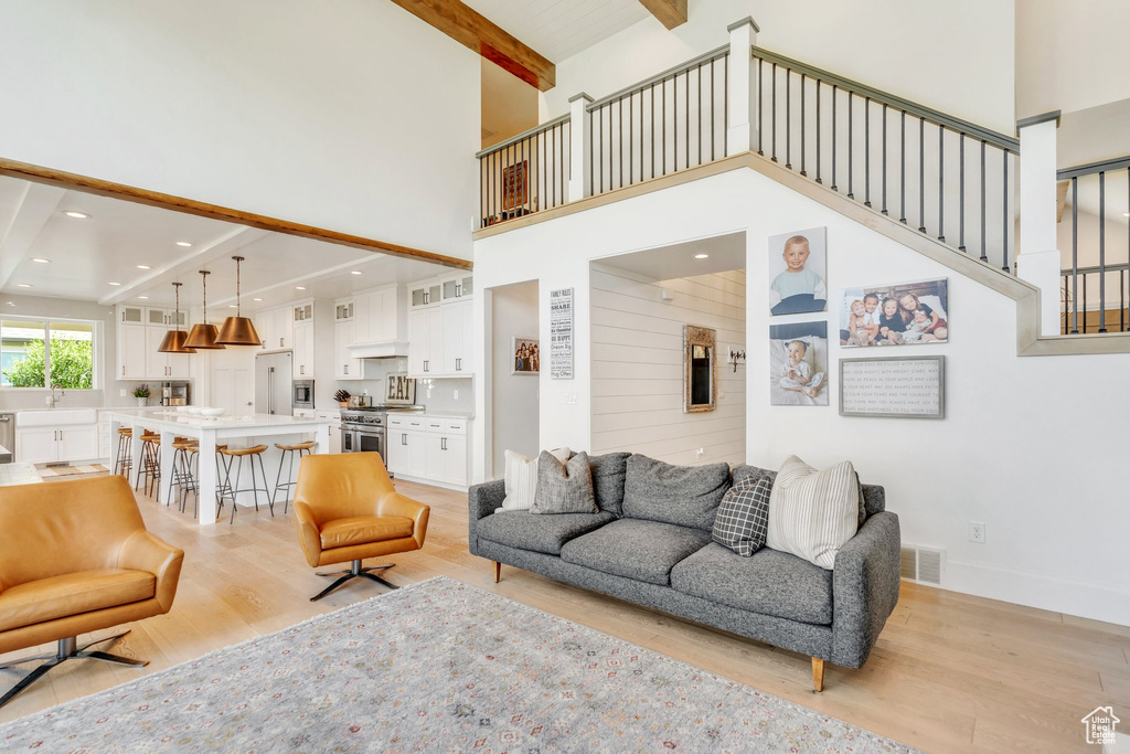 Living area featuring a towering ceiling, light wood finished floors, beamed ceiling, stairs, and recessed lighting