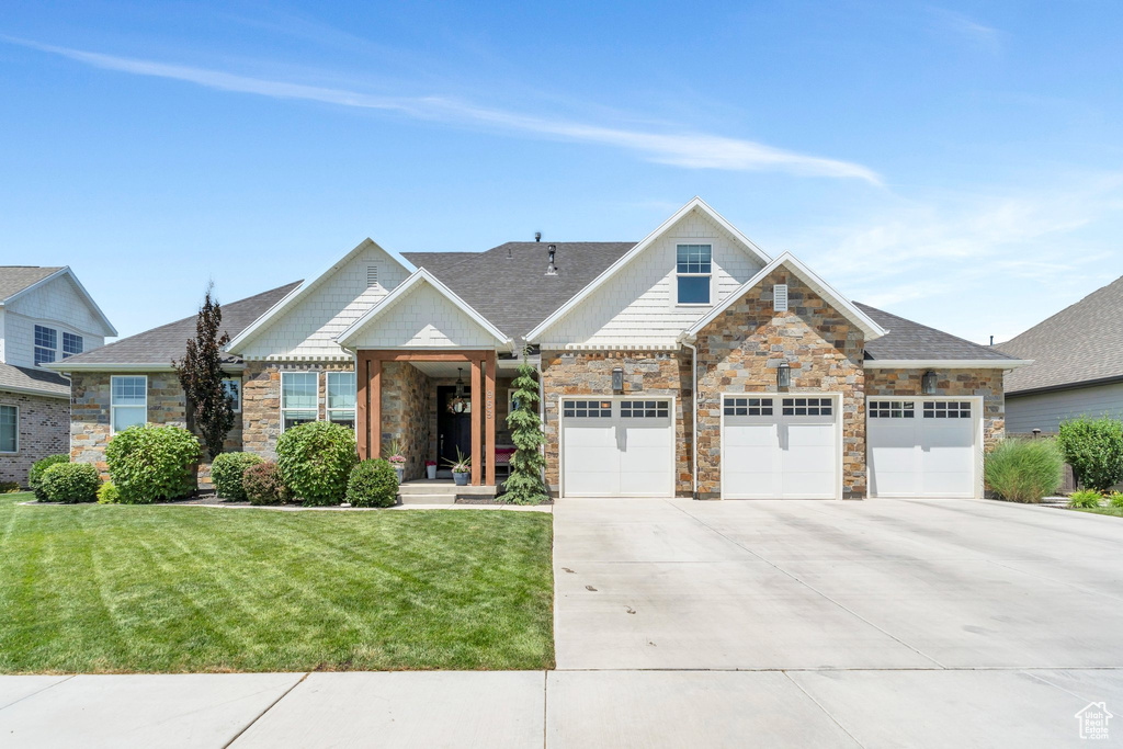 View of front of property featuring driveway, stone siding, a front yard, and an attached garage