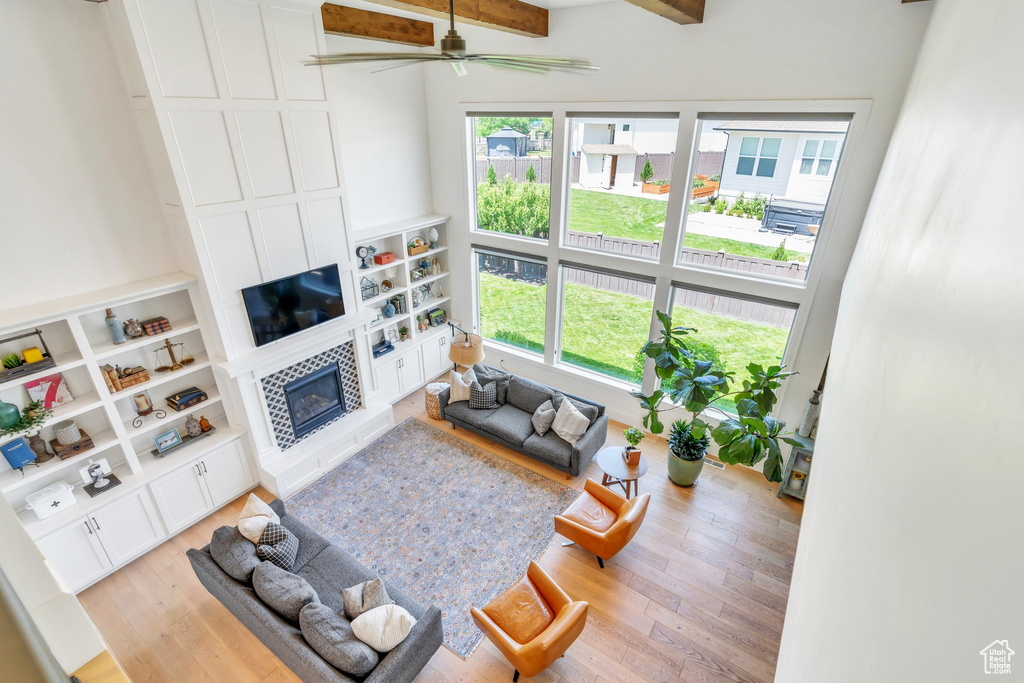 Living room with plenty of natural light, a tiled fireplace, light wood-style flooring, ceiling fan, and beam ceiling