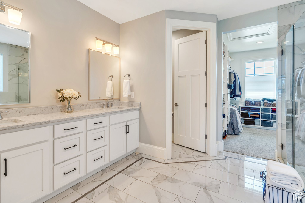 Full bathroom with double vanity, marble look tiles, a walk in closet, and a shower with shower door