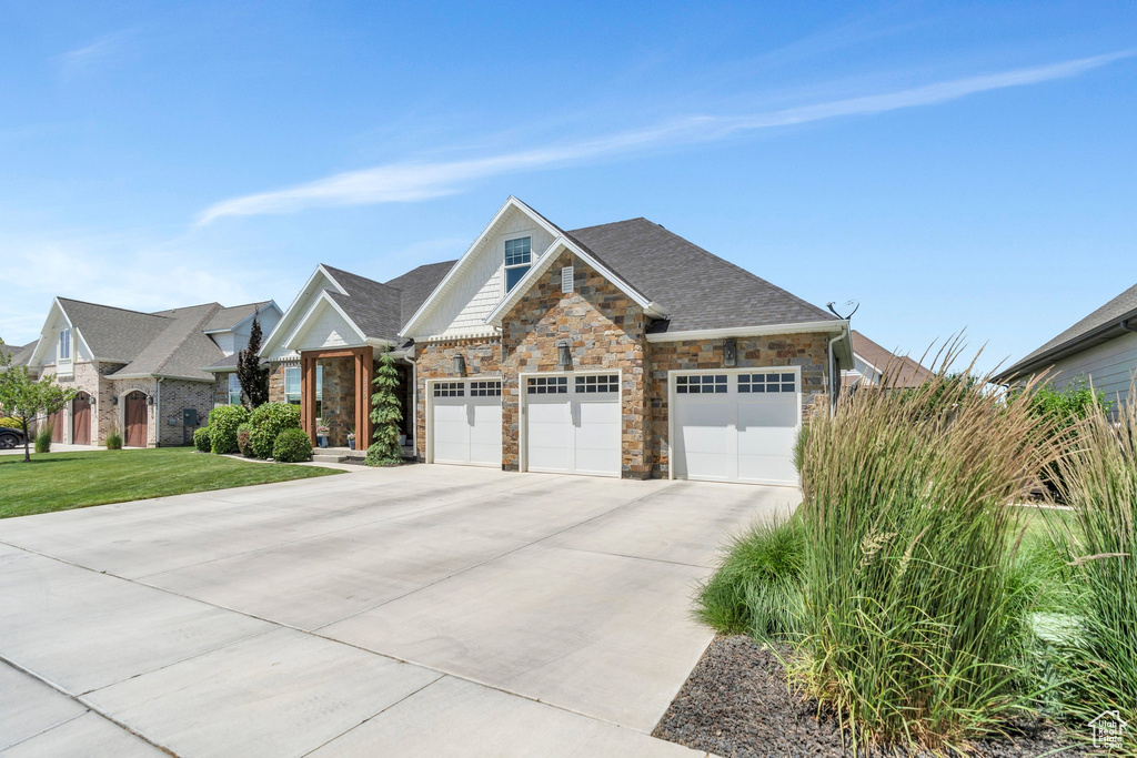 View of front facade featuring driveway, stone siding, a garage, and a front yard