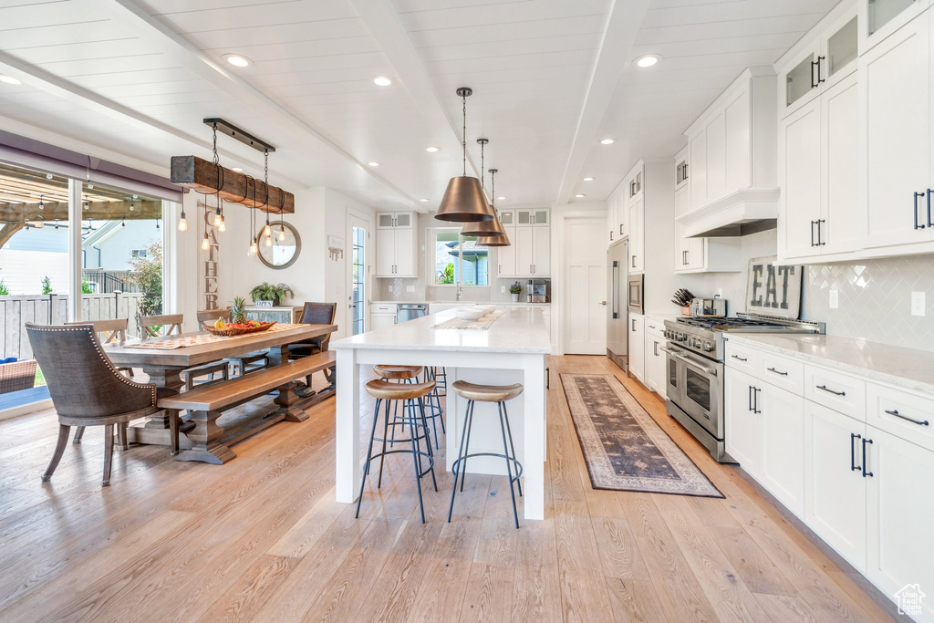 Kitchen featuring range with two ovens, light wood finished floors, tasteful backsplash, a kitchen island, and beam ceiling