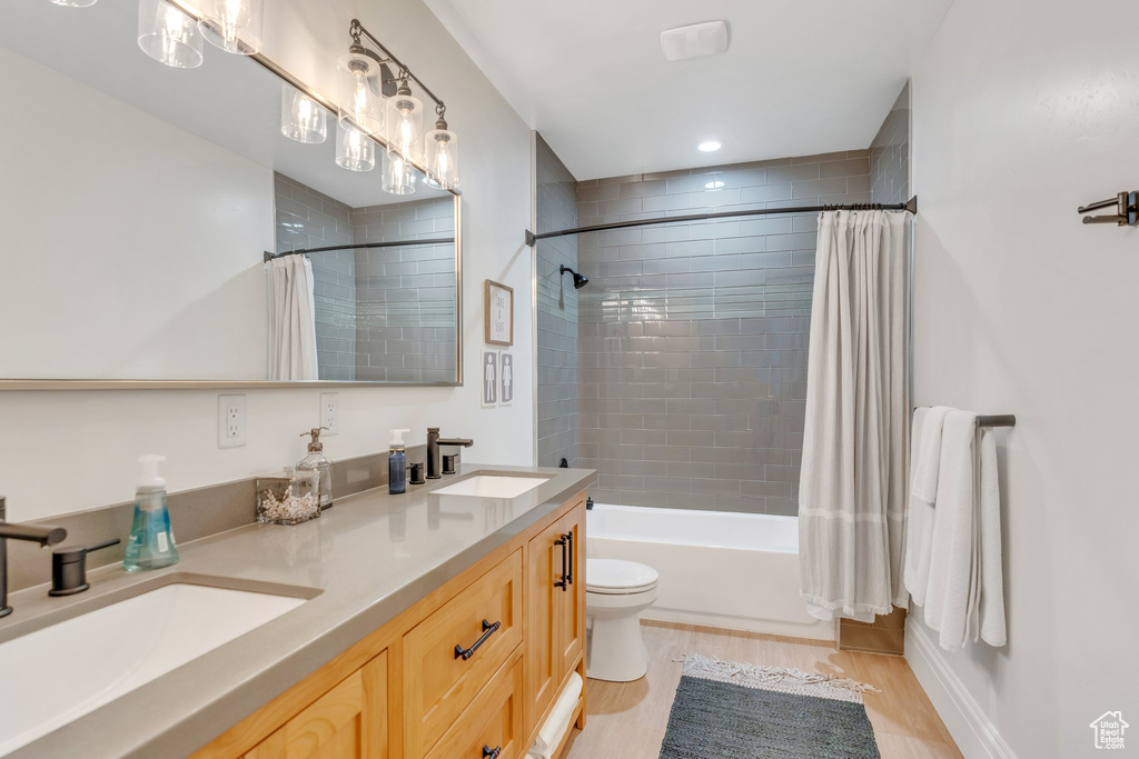 Full bathroom featuring double vanity, shower / bath combo with shower curtain, and wood finished floors