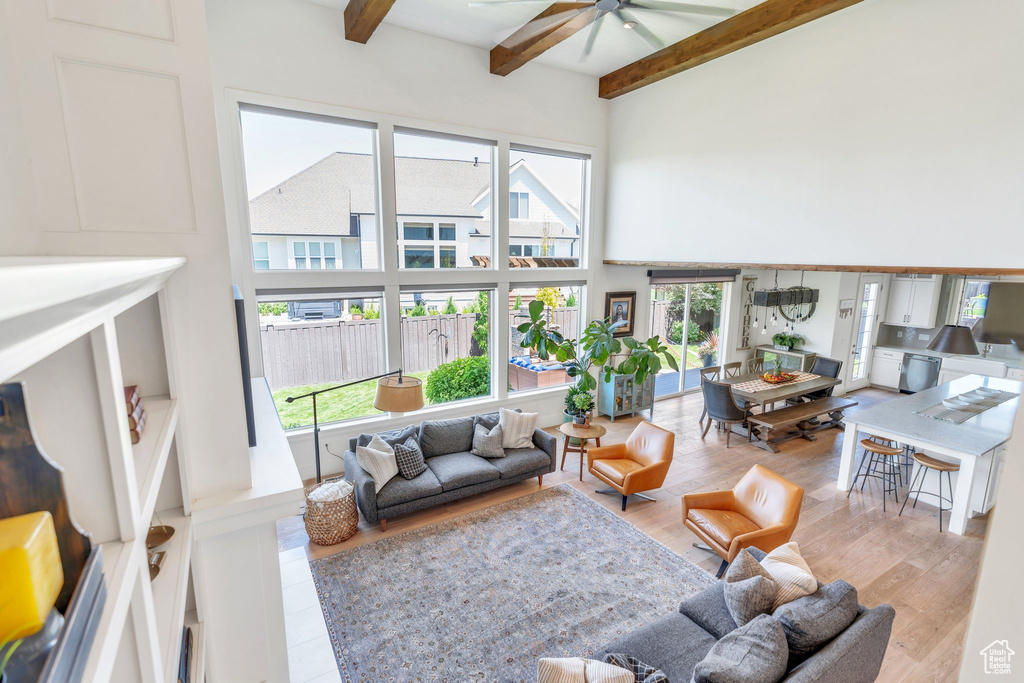 Living room featuring a high ceiling, a ceiling fan, beam ceiling, and wood finished floors