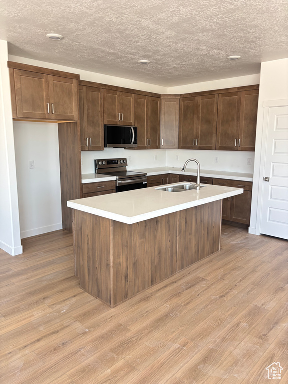 Kitchen with stainless steel range with electric cooktop, light wood-style flooring, light countertops, an island with sink, and a textured ceiling