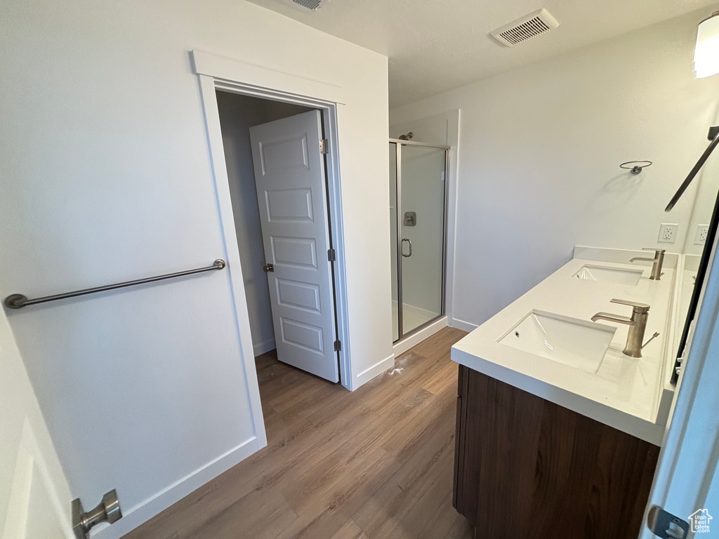 Bathroom featuring a shower stall, double vanity, and wood finished floors
