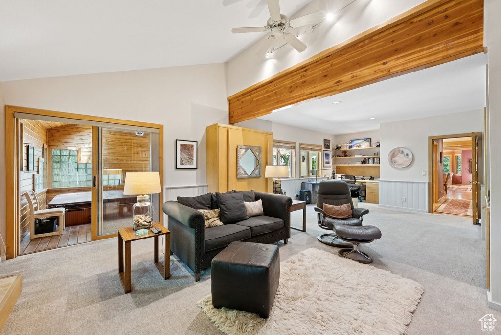 Carpeted living room featuring vaulted ceiling, ceiling fan, and a wainscoted wall
