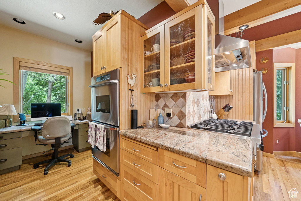 Kitchen with stainless steel double oven, backsplash, light wood-style floors, stove, and light stone counters