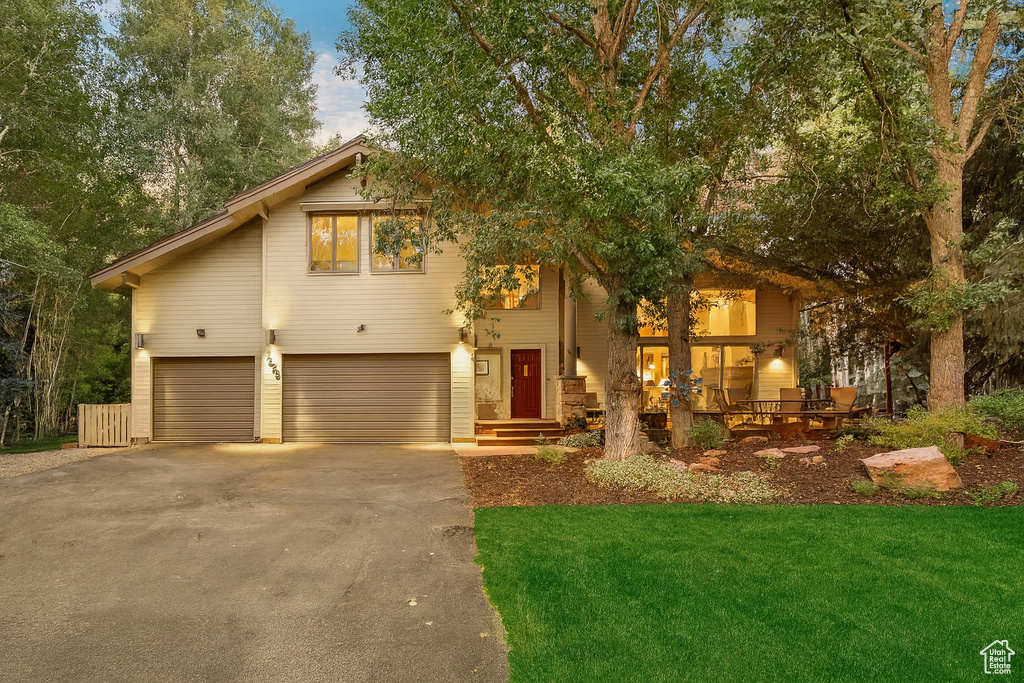 View of front of house with asphalt driveway, an attached garage, and a front yard