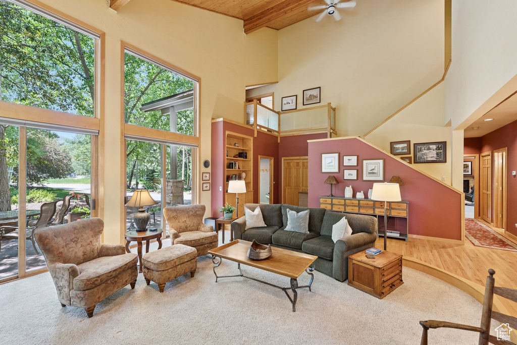 Living room featuring a high ceiling, plenty of natural light, ceiling fan, a wood ceiling with exposed beams, and wood finished floors