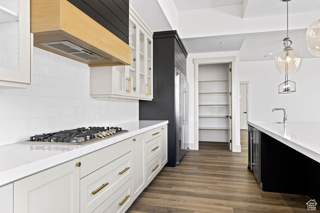 Kitchen featuring ventilation hood, stainless steel gas stovetop, light countertops, glass insert cabinets, and hanging light fixtures