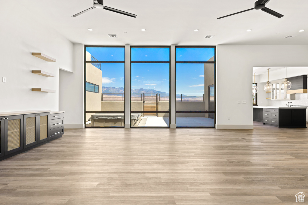 Unfurnished living room featuring a ceiling fan, light wood-type flooring, a wall of windows, healthy amount of natural light, and recessed lighting