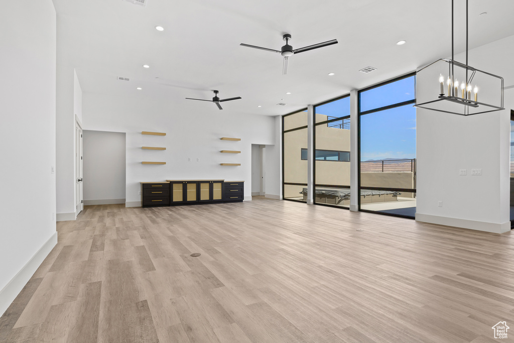 Unfurnished living room featuring a ceiling fan, a wall of windows, light wood-type flooring, recessed lighting, and a chandelier