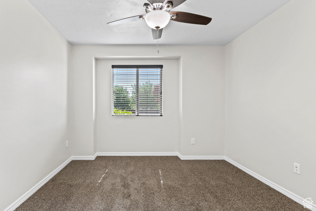 Unfurnished room featuring dark colored carpet and a ceiling fan
