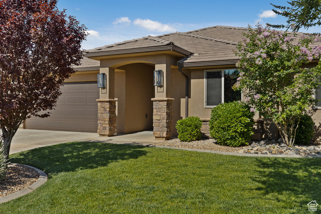 View of front of house featuring stucco siding, an attached garage, a front yard, a tiled roof, and driveway