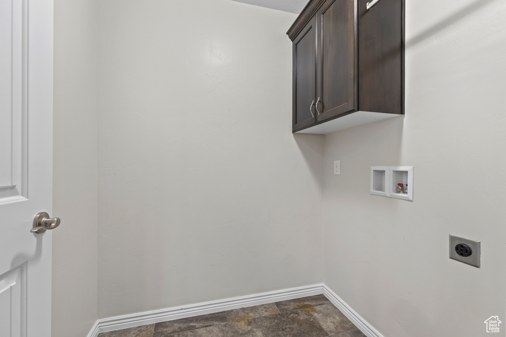 Washroom featuring hookup for an electric dryer, cabinet space, washer hookup, and dark stone finish floors