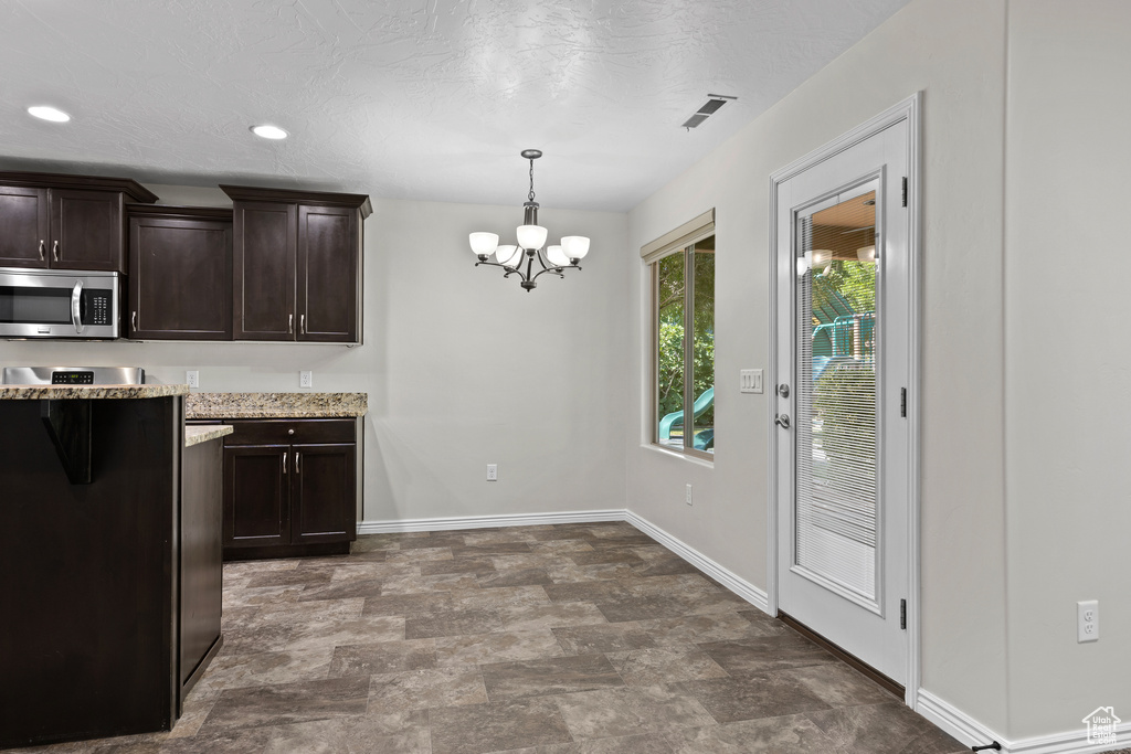 Kitchen with stainless steel microwave, a chandelier, dark brown cabinets, stone finish flooring, and light stone counters