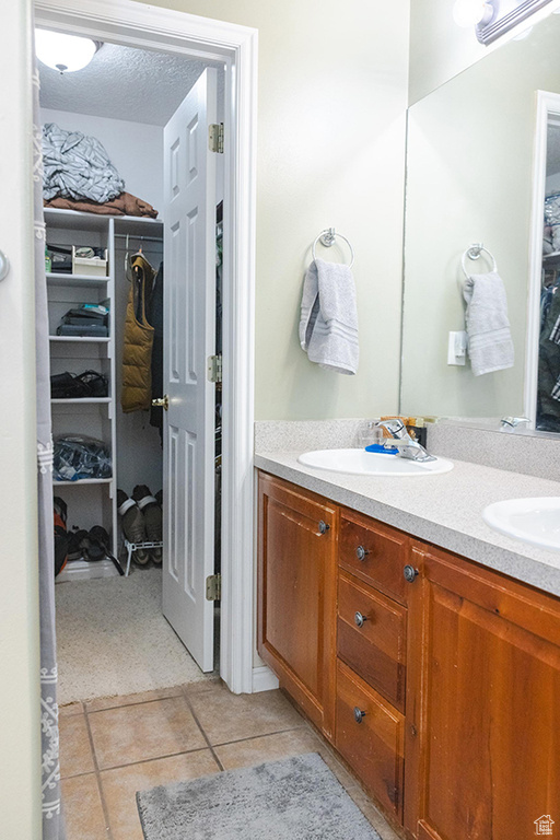 Full bath featuring double vanity, a walk in closet, and tile patterned floors