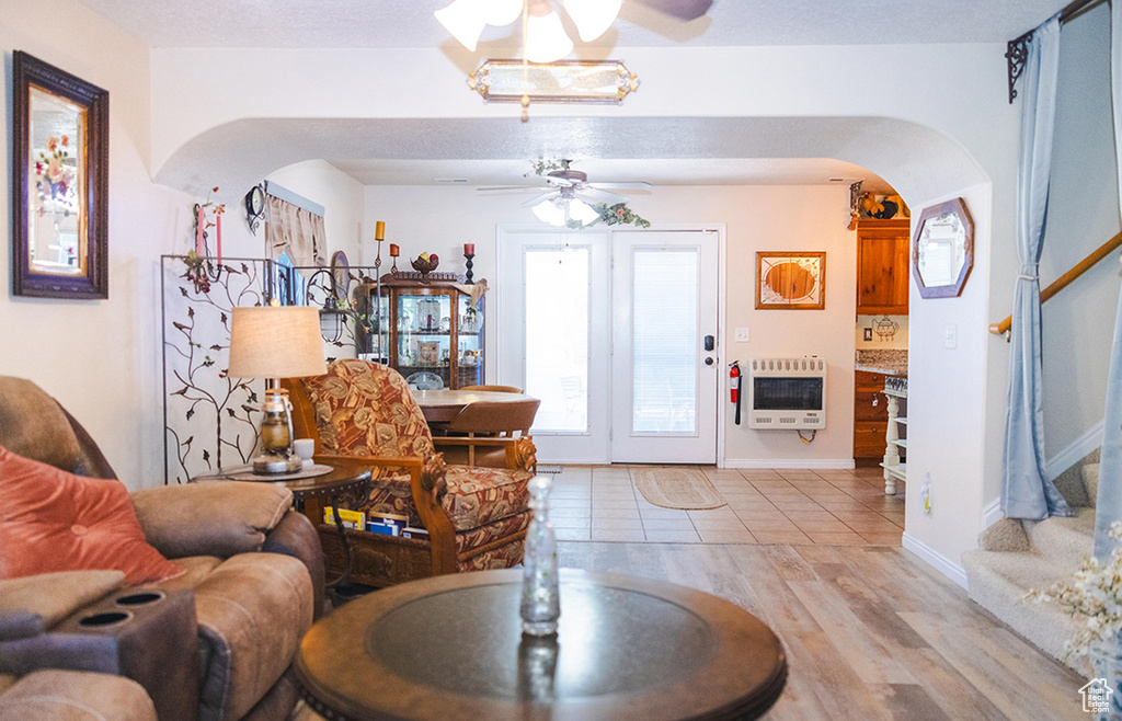 Living area with heating unit, arched walkways, ceiling fan, stairway, and light wood-style floors