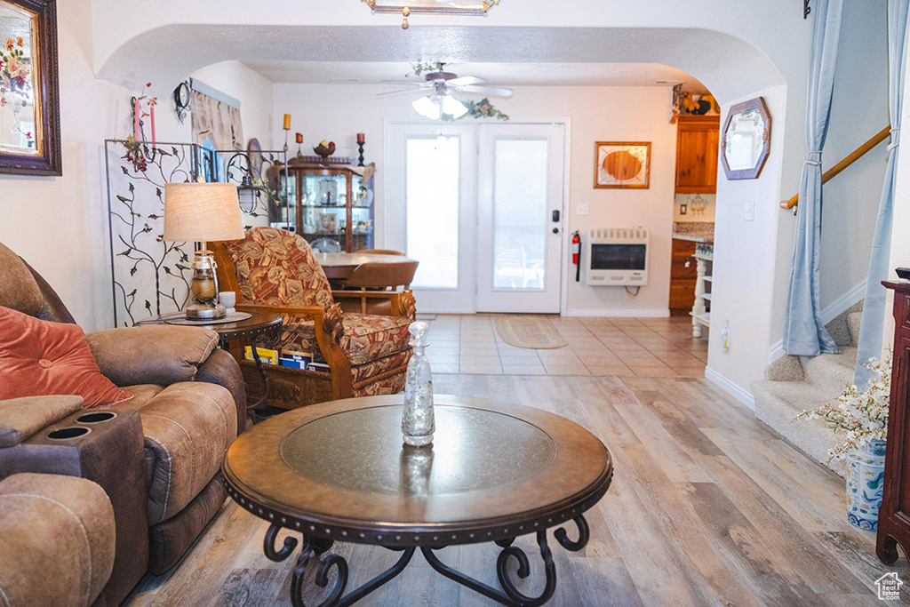 Living area with arched walkways, heating unit, a ceiling fan, light wood finished floors, and stairway