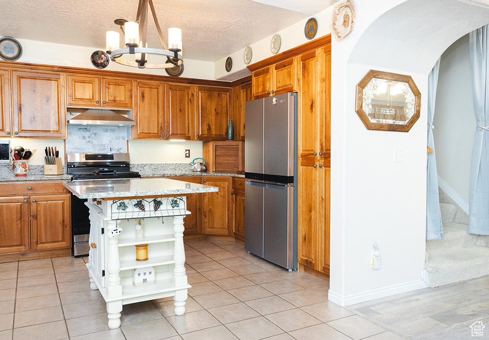 Kitchen with appliances with stainless steel finishes, open shelves, under cabinet range hood, a chandelier, and brown cabinetry