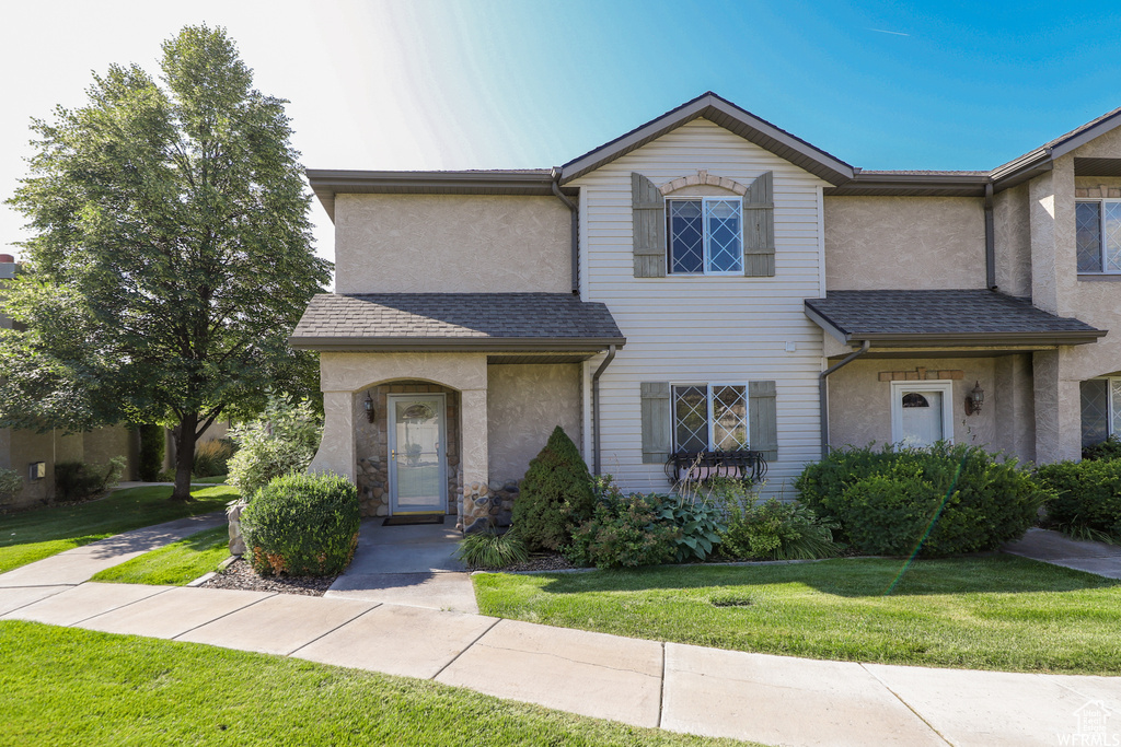 View of front facade featuring stucco siding, a front yard, and a shingled roof