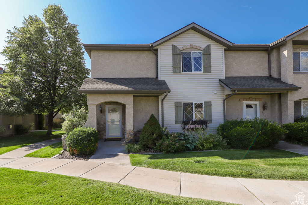 View of front facade with stucco siding, a front yard, and a shingled roof
