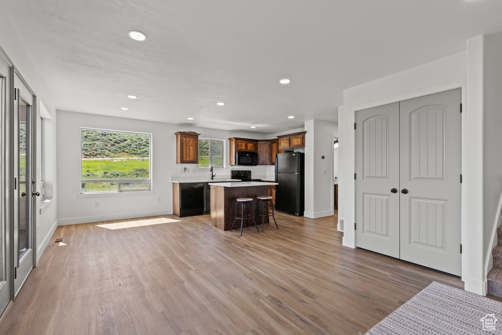 Kitchen featuring black appliances, a kitchen island, recessed lighting, light wood-style floors, and a kitchen breakfast bar