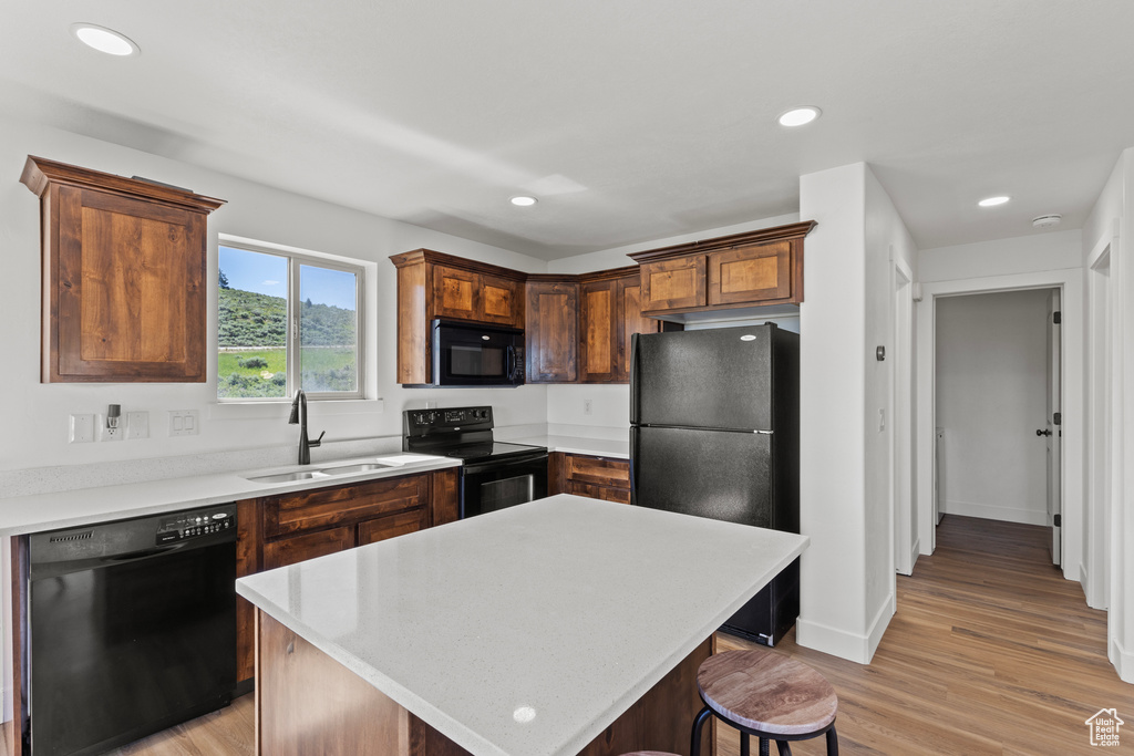 Kitchen featuring black appliances, light countertops, light wood finished floors, a kitchen bar, and recessed lighting