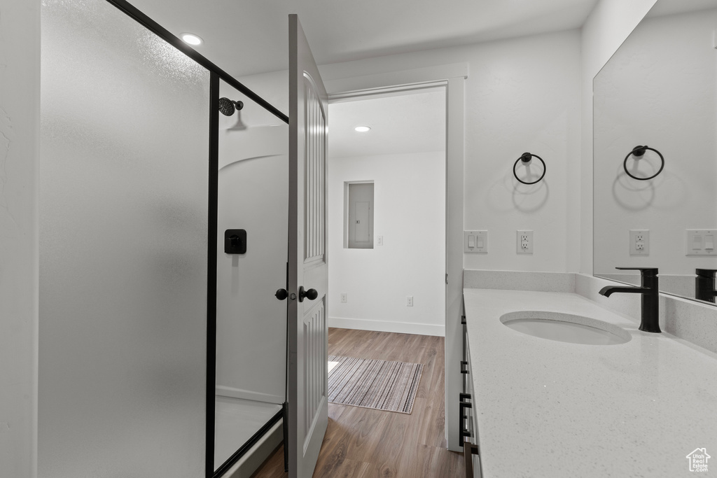 Bathroom featuring vanity, a walk in shower, wood finished floors, and recessed lighting