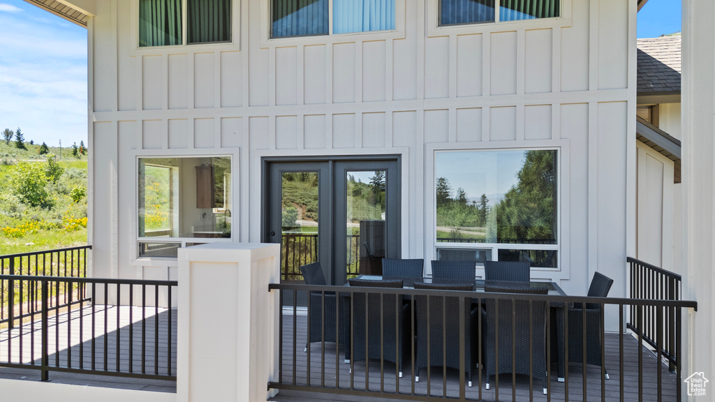 View of exterior entry featuring board and batten siding, a shingled roof, outdoor dining area, and a deck