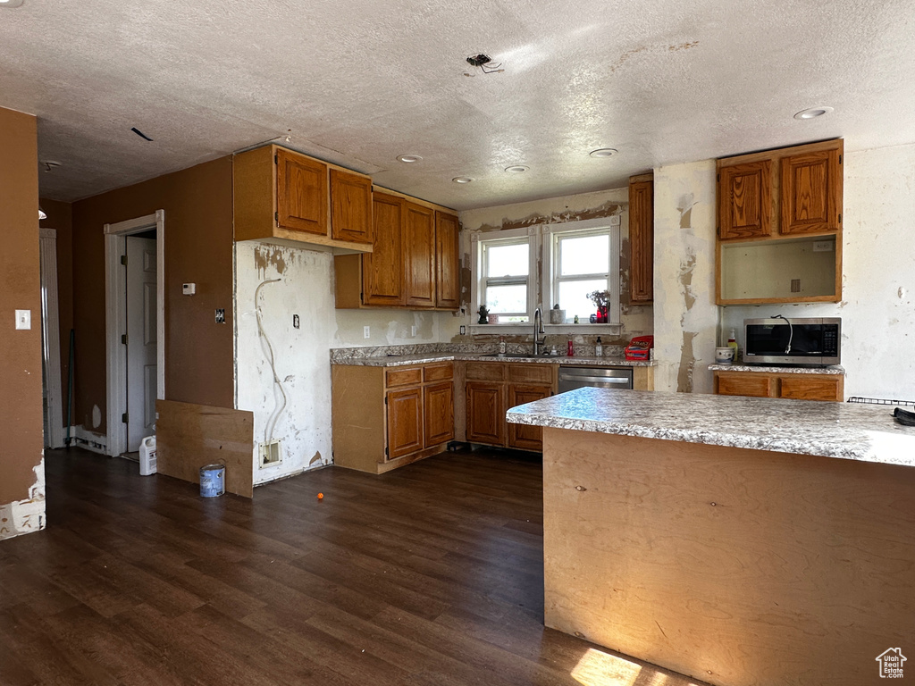 Kitchen featuring stainless steel appliances, dark wood finished floors, brown cabinets, a textured ceiling, and recessed lighting