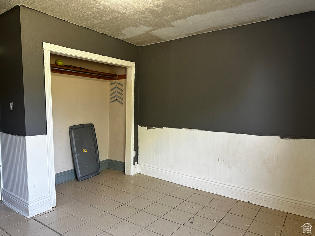 Unfurnished bedroom featuring a wainscoted wall, light tile patterned floors, and a closet