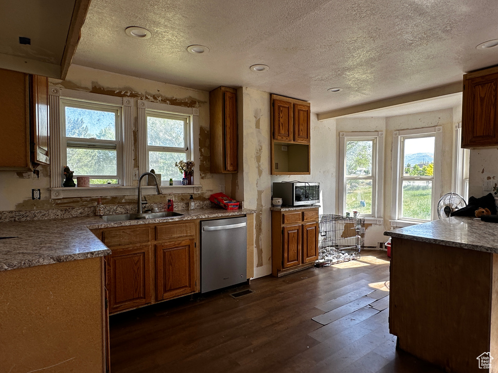 Kitchen with appliances with stainless steel finishes, a textured ceiling, dark wood-style floors, plenty of natural light, and brown cabinets