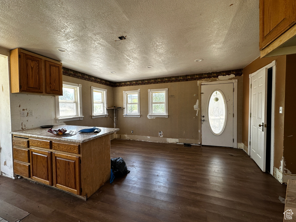 Kitchen with a textured ceiling, dark wood-type flooring, brown cabinets, a peninsula, and light countertops