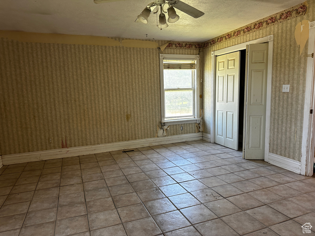 Unfurnished room featuring wallpapered walls, ceiling fan, a textured ceiling, and light tile patterned floors