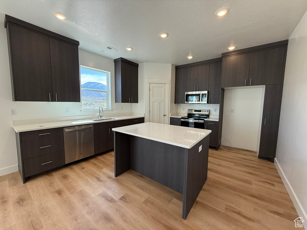 Kitchen featuring stainless steel appliances, light countertops, a kitchen island, light wood-style flooring, and a textured ceiling
