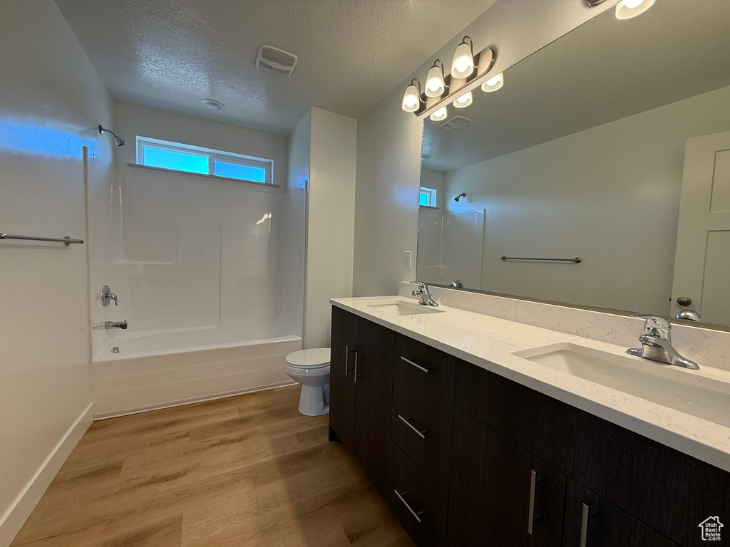 Full bath featuring tub / shower combination, double vanity, wood finished floors, and a textured ceiling