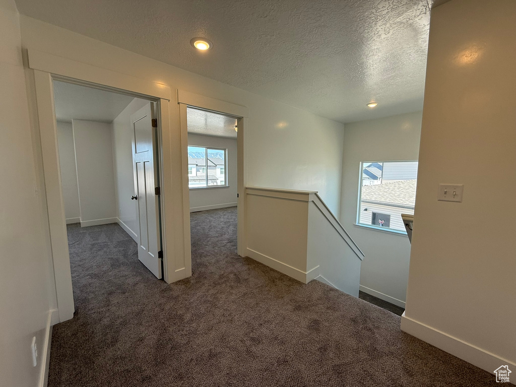 Hall featuring dark carpet, an upstairs landing, a textured ceiling, and recessed lighting