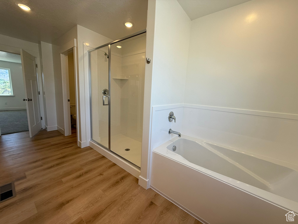 Bathroom with a garden tub, a shower stall, wood finished floors, and recessed lighting