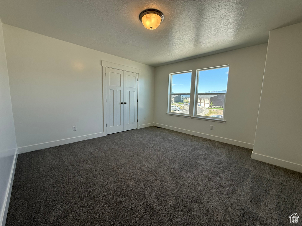 Unfurnished bedroom with dark colored carpet, a textured ceiling, and a closet