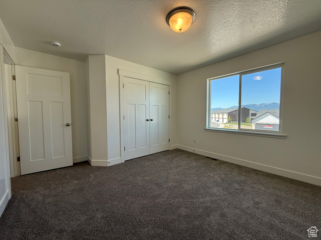 Unfurnished bedroom featuring dark colored carpet, a textured ceiling, and a closet