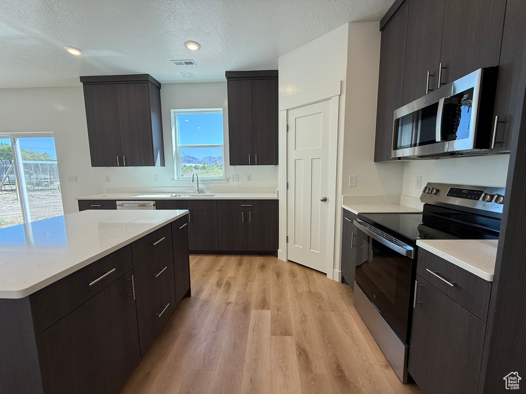 Kitchen featuring stainless steel appliances, light countertops, a textured ceiling, light wood-style flooring, and modern cabinets