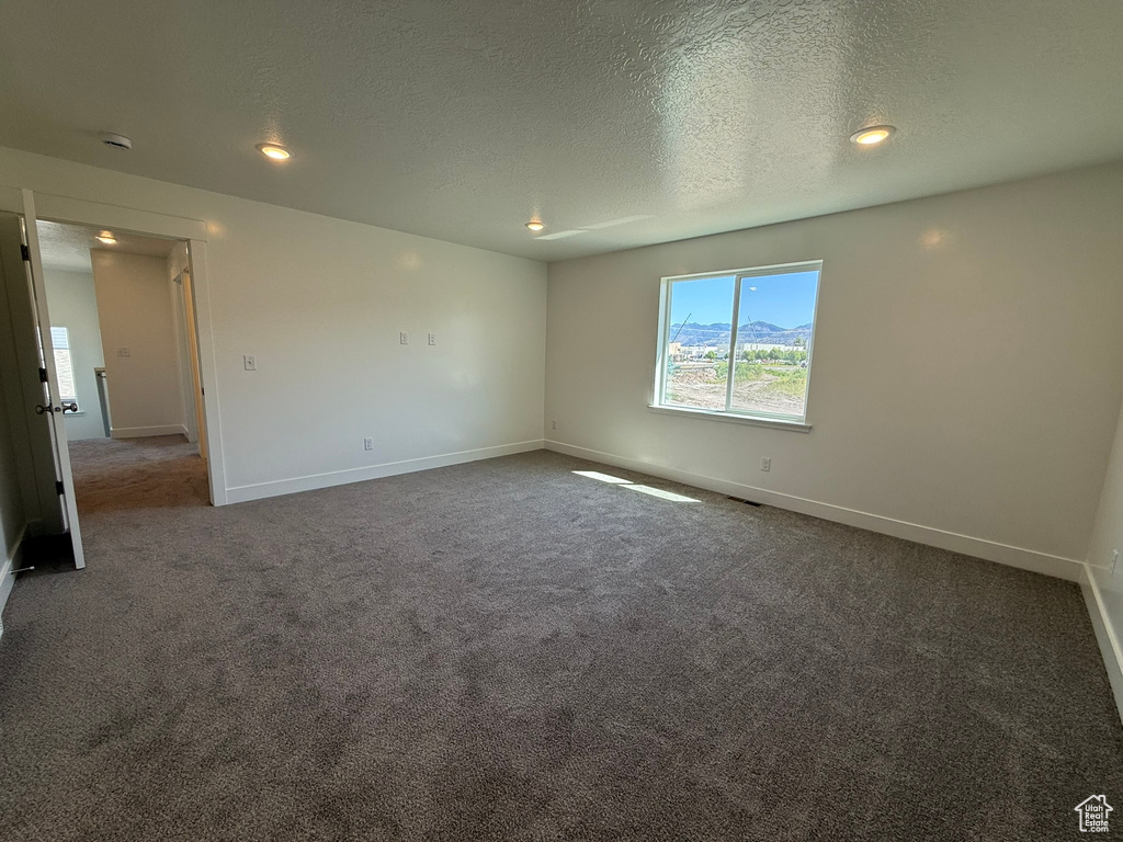 Empty room featuring dark carpet, a textured ceiling, recessed lighting, and a smoke detector