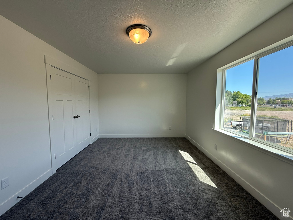 Unfurnished bedroom featuring dark carpet and a textured ceiling