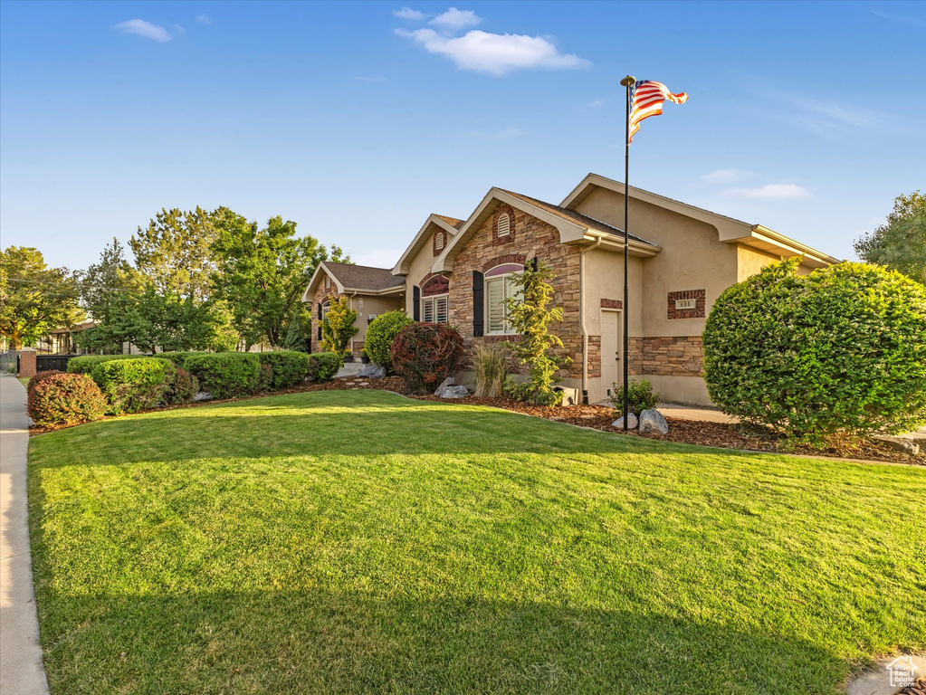 View of front of house with stone siding, a front yard, and stucco siding