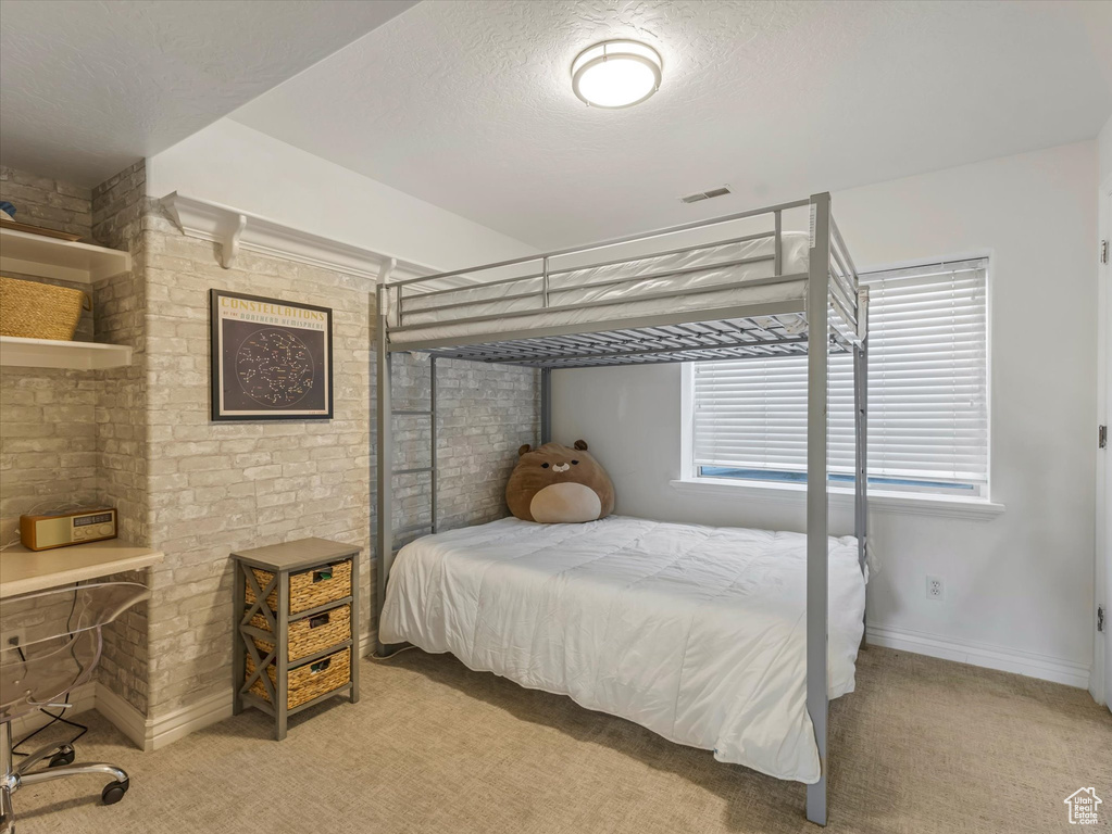 Bedroom featuring light colored carpet, brick wall, and a textured ceiling