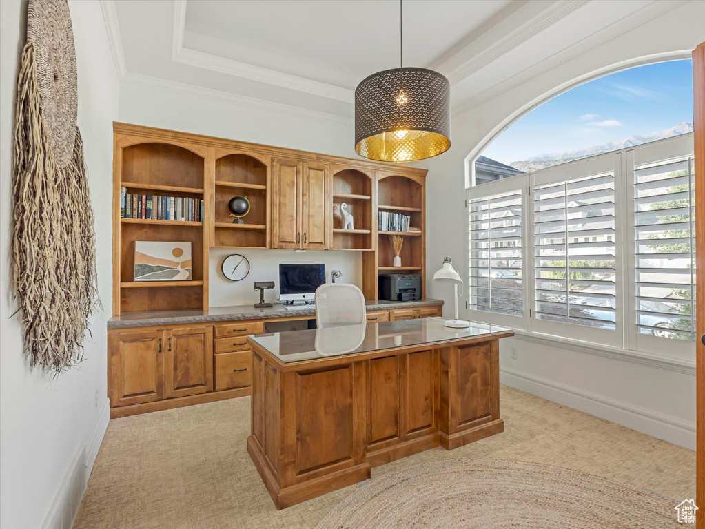 Office space with a tray ceiling, light colored carpet, built in study area, and crown molding