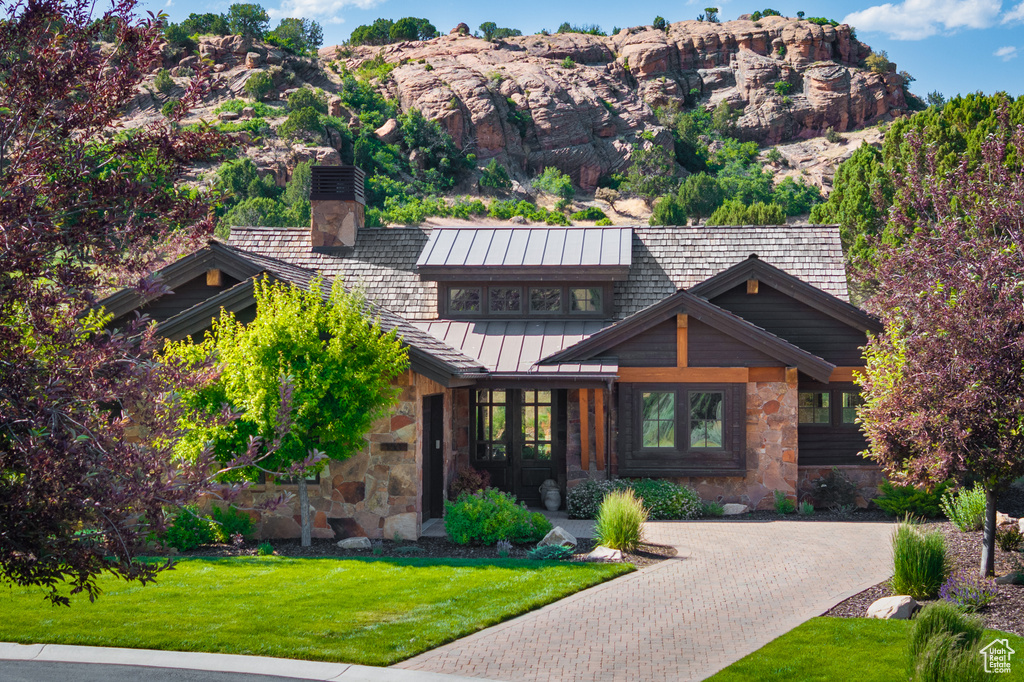 View of front of property featuring a standing seam roof, stone siding, a front yard, and a chimney
